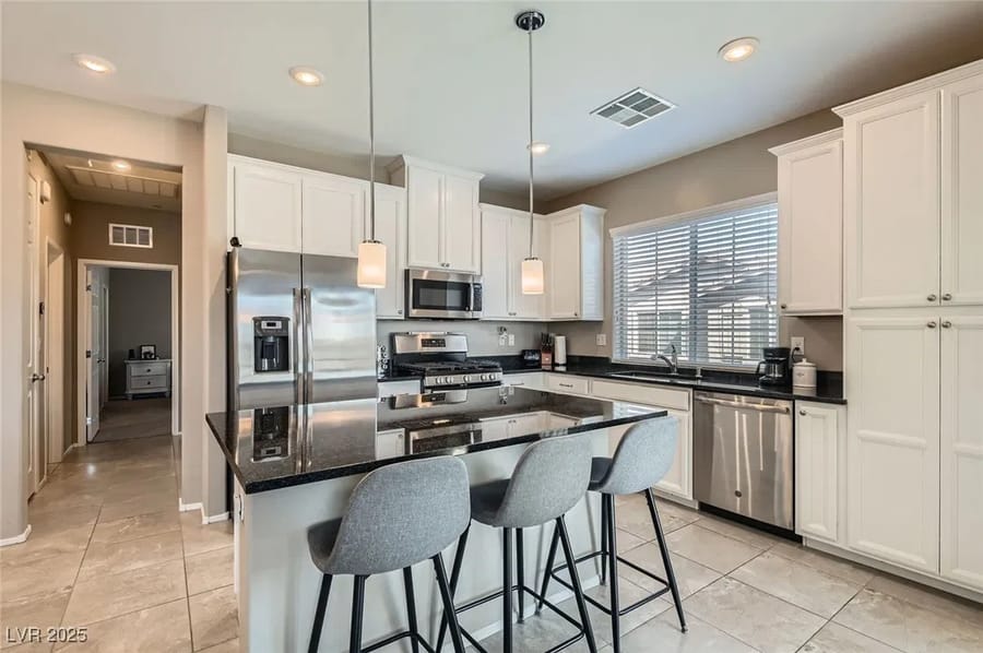 Cocina blanca con isla y lámparas colgantes en una casa vendida por Park Place Realty, Las Vegas